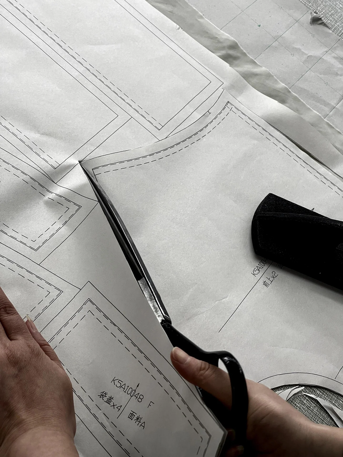 Hands cutting marked paper pattern pieces with shears.