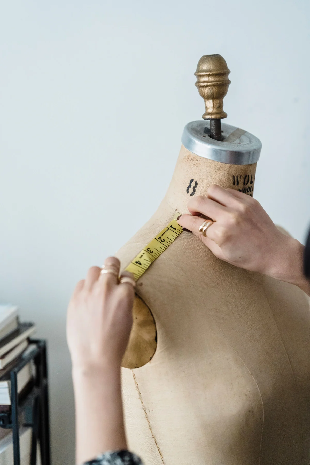Hands using a measuring tape across the shoulder of a dress form.